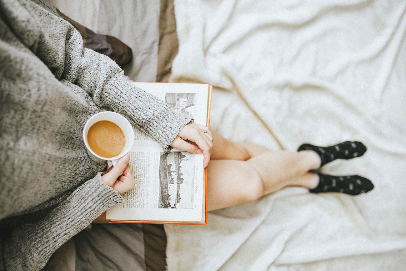 Reading a book in bed whilst holding a coffee