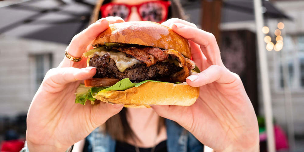 Hands holding a burger at Apex Temple Court Hotel