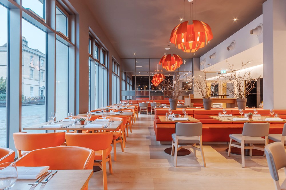 Restaurant at Apex City of Bath Hotel with orange chairs, wooden tables and lights