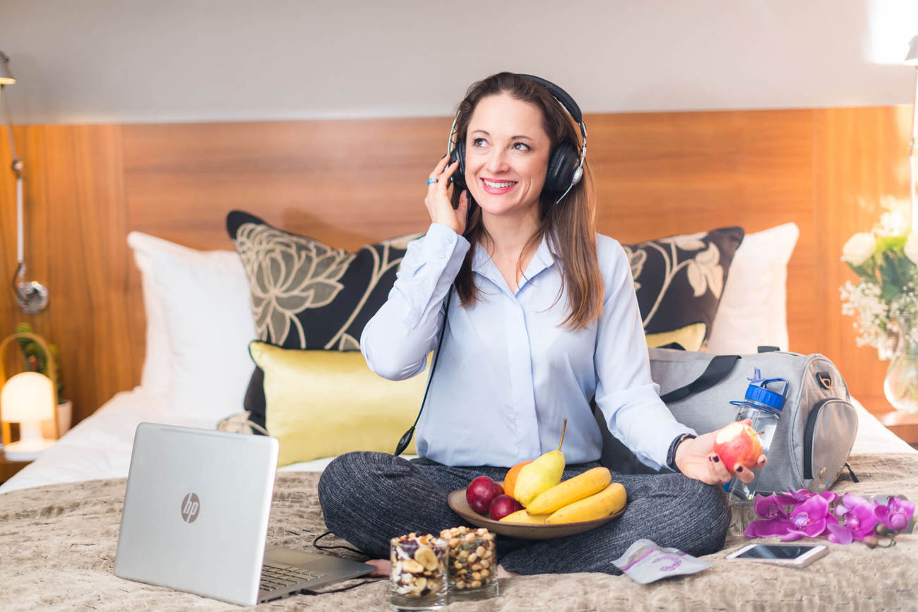 Celynn Morin at Apex Hotels Celynn Morin sitting on bed listening to podcast with headphones on