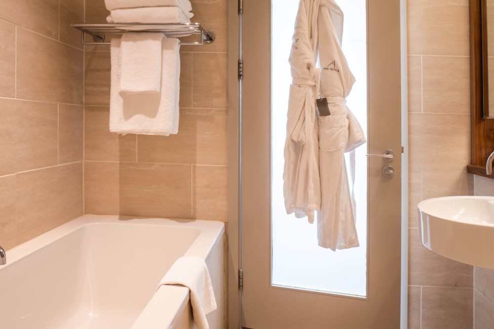 Family Room bathroom with bath and robes hanging on door at Apex Waterloo Place Hotel