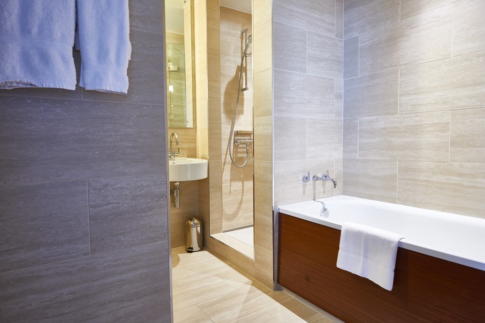 Deluxe Room bathroom with bath and walk-in shower at Apex City of London Hotel